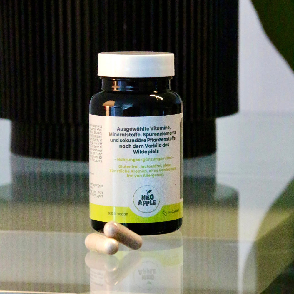 Neoapple Vitaminkapseln und Flasche auf einem spiegelnden Glastisch vor einem dunklen Hintergrund