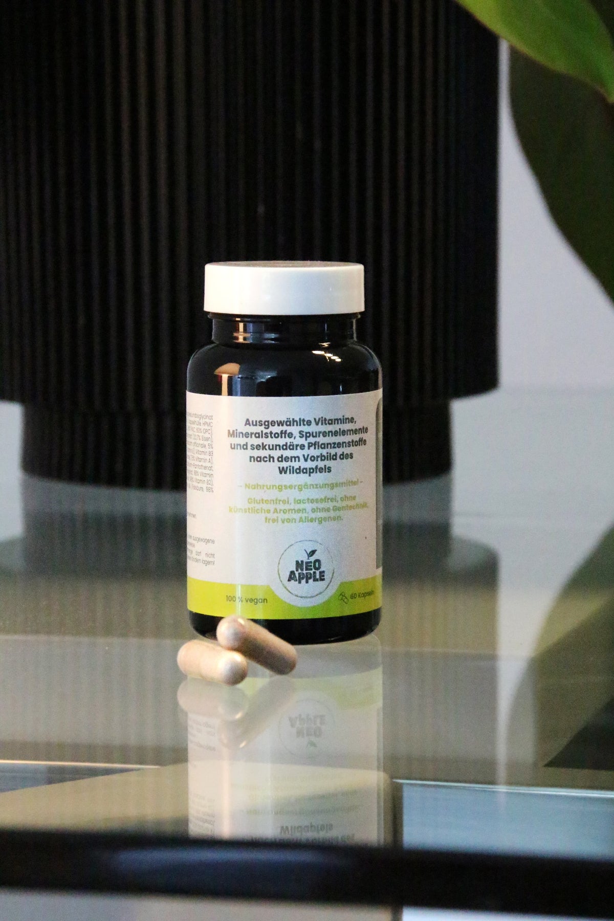 Neoapple Vitaminkapseln und Flasche auf einem spiegelnden Glastisch vor einem dunklen Hintergrund