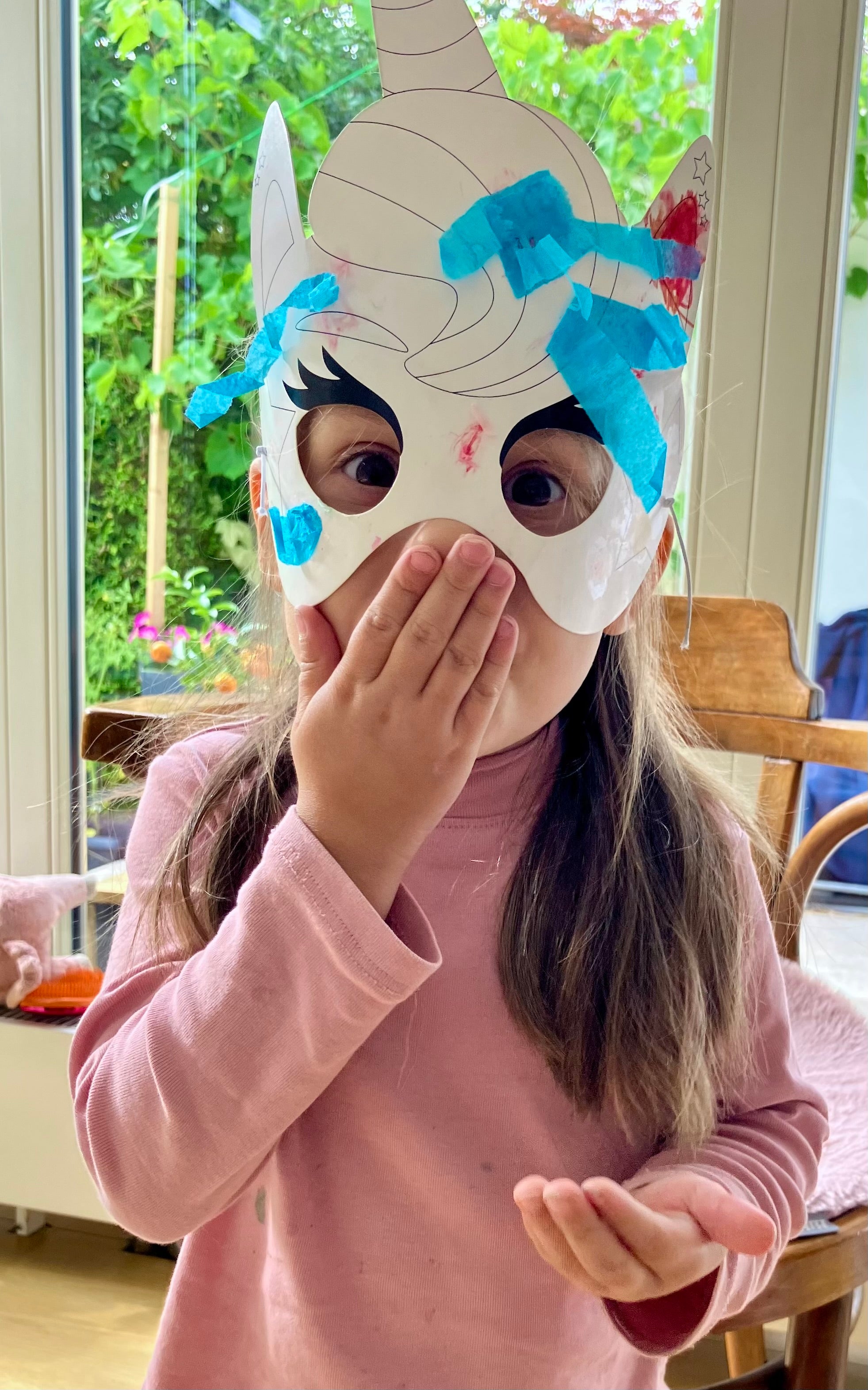 Kleines Mädchen mit Papiermaske vor dem Gesicht 