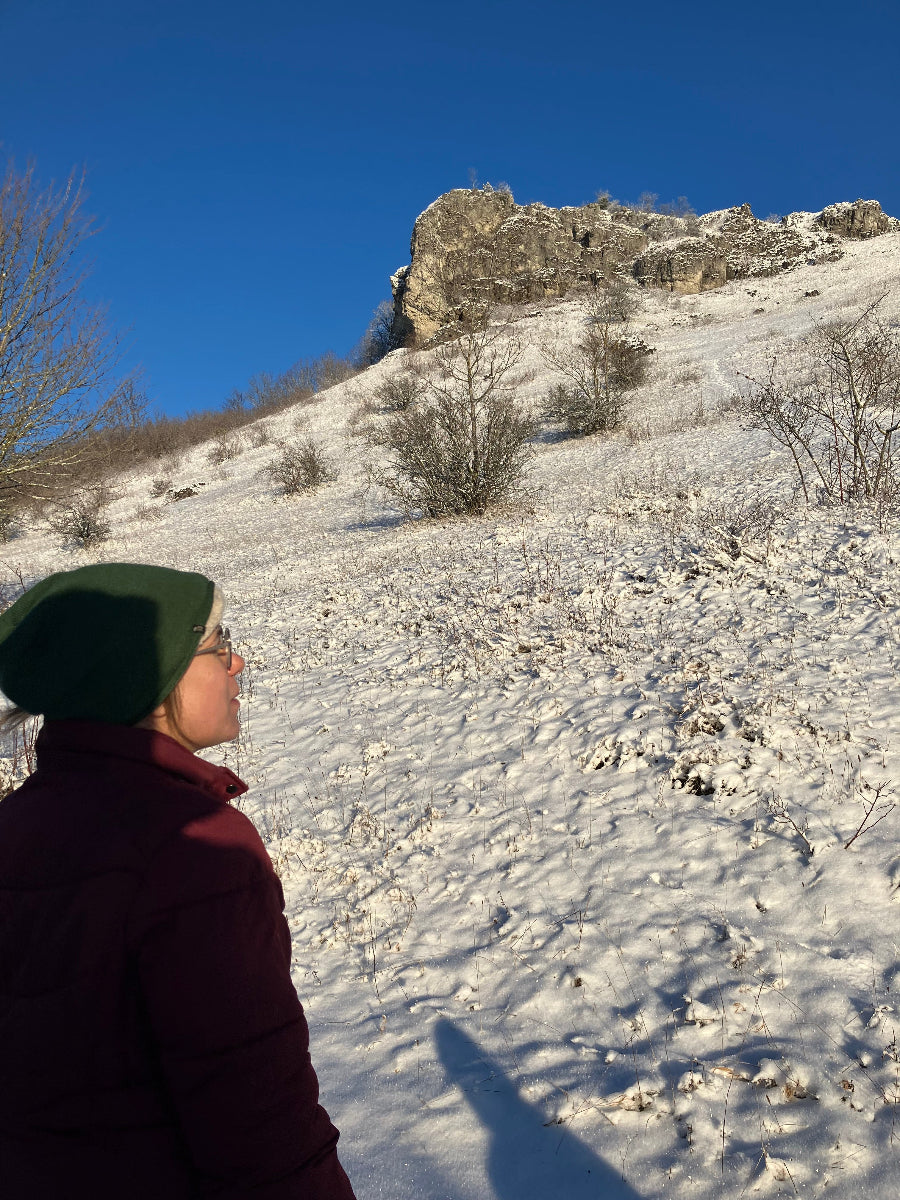 Frau in Winterkleidung schaut auf einen verschneiten Berg mit einer felsigen Spitze.