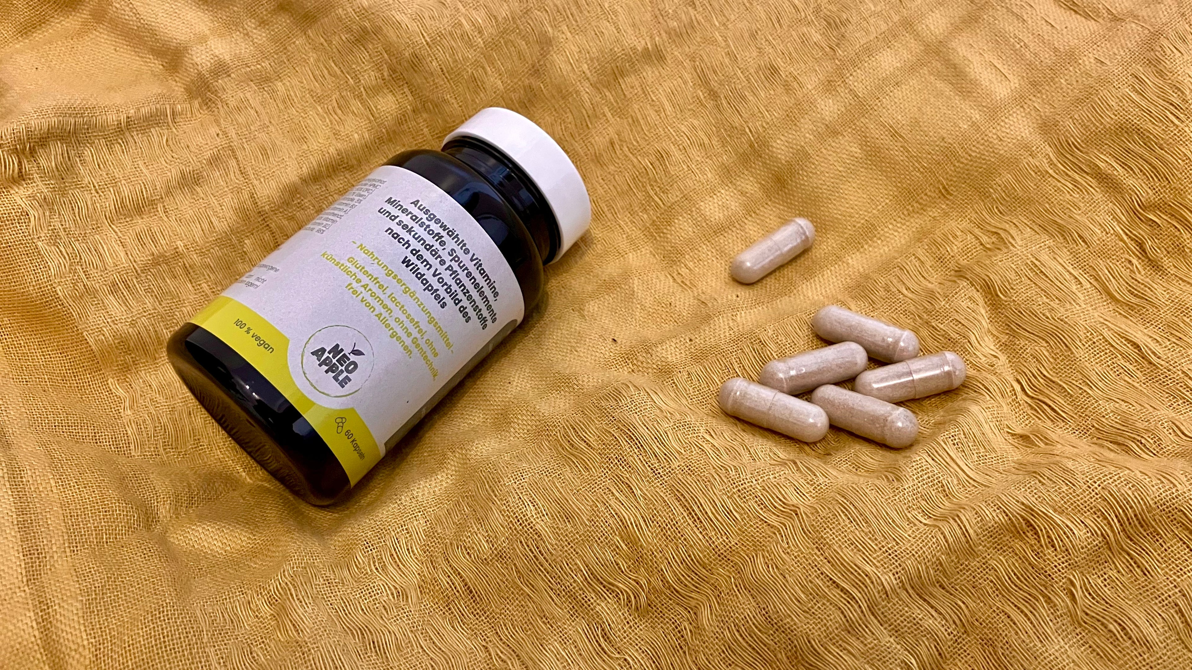 Neoapple Kapseln Dose von Neoapple mit Vitaminen für das Immunsystem und den Energiestoffwechsel auf einem gelben Stofftuch