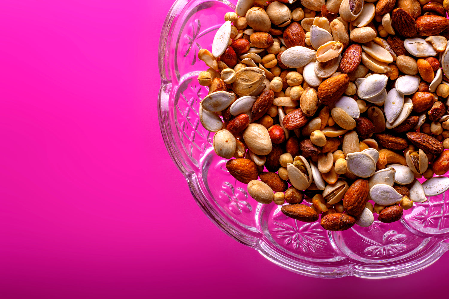Nuss-Mischung mit Mandeln, Cashews und anderen Nüssen und Kernen, die Magnesium enthalten in einer Glasschüssel auf einem pinkfarbenen Untergrund