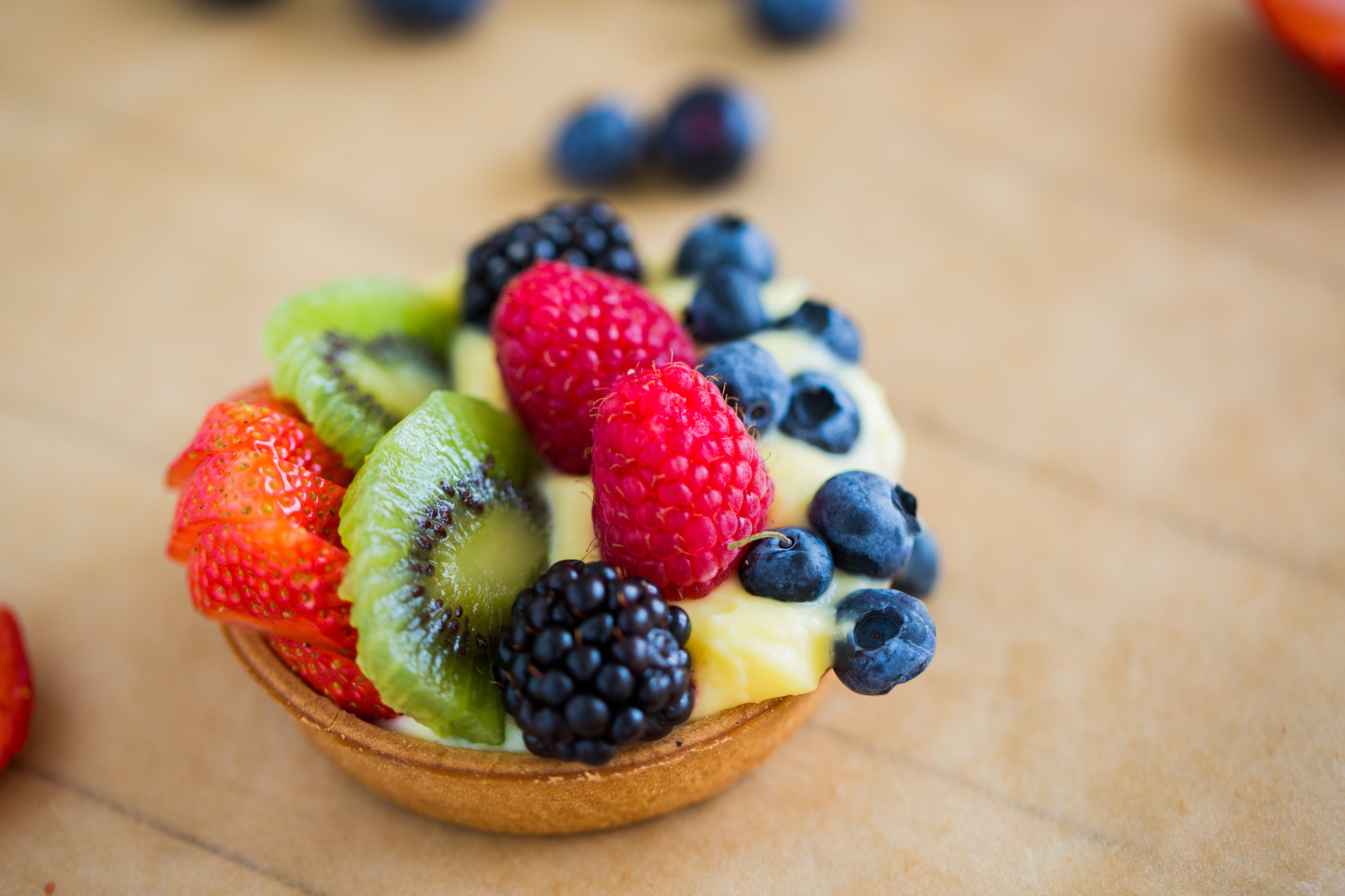 Obsttörtchen mit Himbeeren, Brombeeren, Erdbeeren, Blaubeeren und Kiwi auf einer hellen Unterlage. Steht symbolisch für Kalorien in Früchten. 