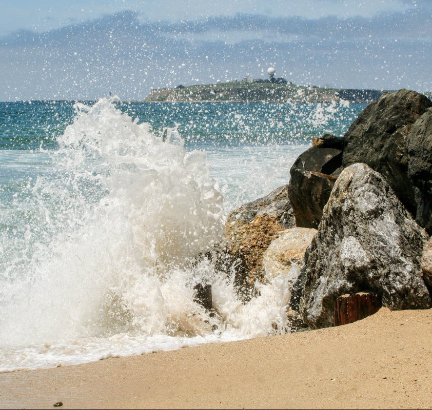 Meeresküste mit Sandstrand und Felsen, Wasser spritzt an den Felsen hoch. Meerwasser enthält viele Mineralien, wie auch Magnesium.