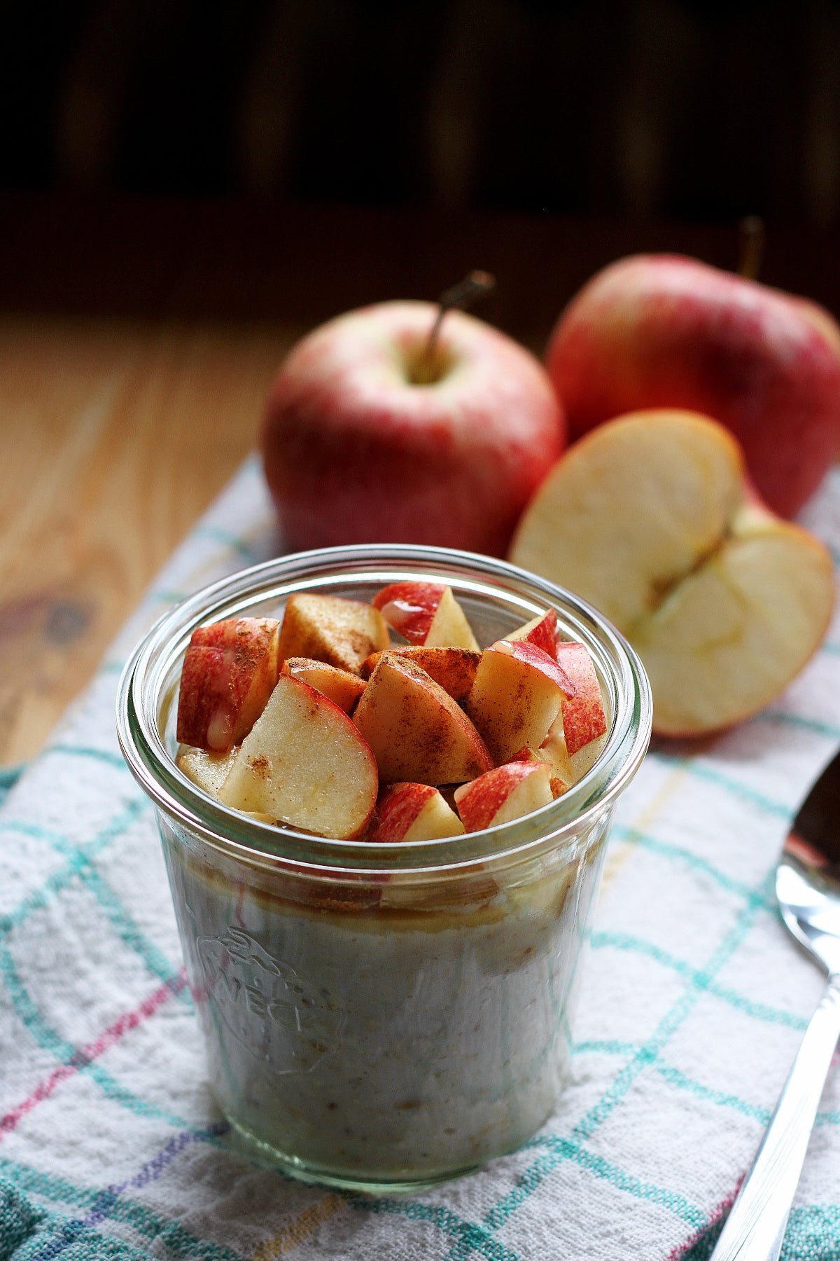 Äpfel und ein Glas mit Joghurt mit Obst auf einem Geschirrtuch auf einem Holztisch