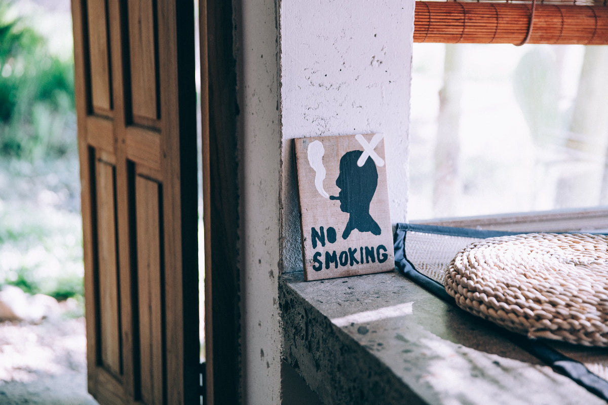 Schild mit der Aufschrift "No Smoking" auf einer steinernen Sitzbank mit einem Kissen. 